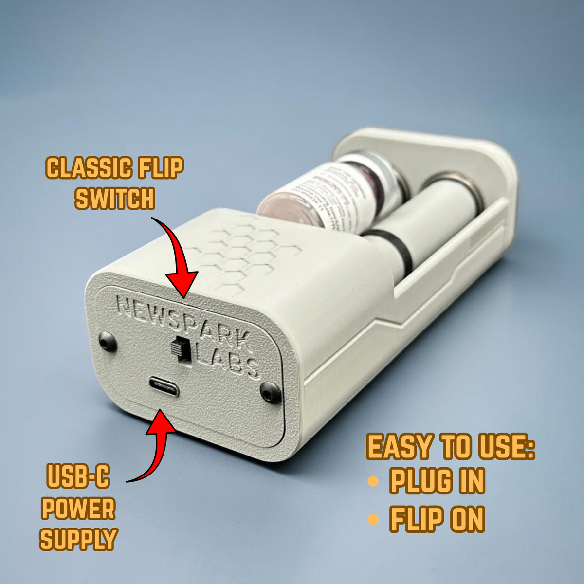 An open, gray motorized vial roller mixer device shown on a blue-gray gradient background. Yellow-orange text reads 'USB-C Power Supply', 'Classic Flip Switch' and 'Easy to Use: Plug In. Flip On.' A small vial with a white label lays in the device between two rollers. A decorative honeycomb motif is etched into the top and there are decorative ridges on the side. 