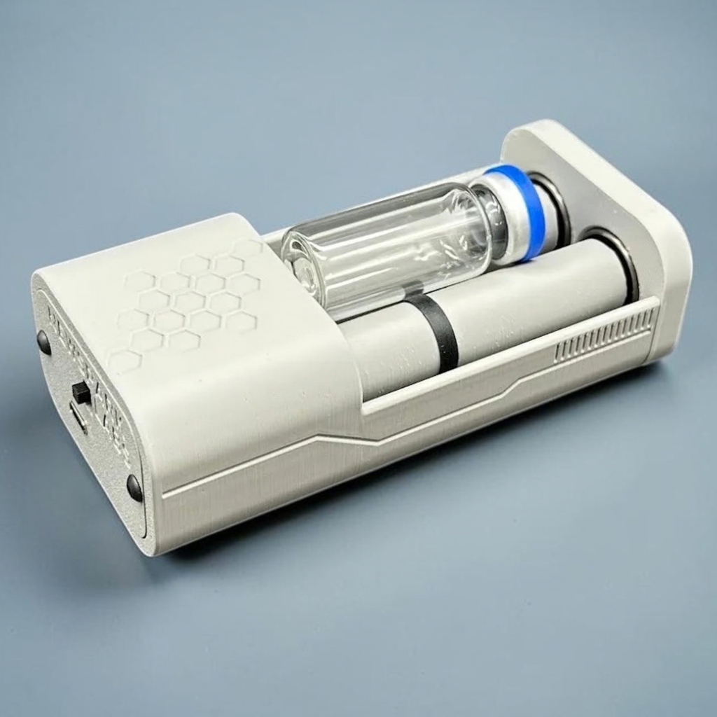 An open, gray, motorized vial roller holder with a medication vial (with a blue cap) nestled between two rollers, set against a blue-gray gradient background.