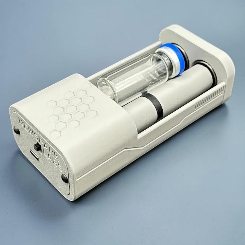 An open, gray, motorized vial roller holder with a medication vial (with a blue cap) nestled between two rollers, set against a blue-gray gradient background.